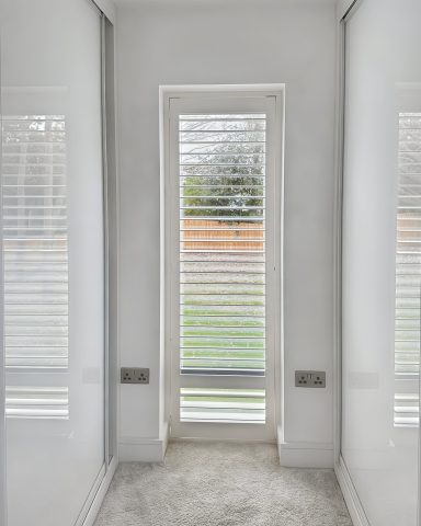 Narrow hallway with white walls and a door leading to an outdoor area with blinds.
