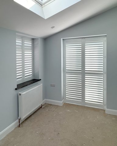 Bright room with light blue walls, wooden shutters, and a radiator beneath a window.