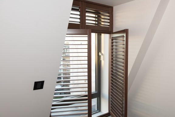 Window with wooden shutters and a slanted wall, allowing natural light indoors.